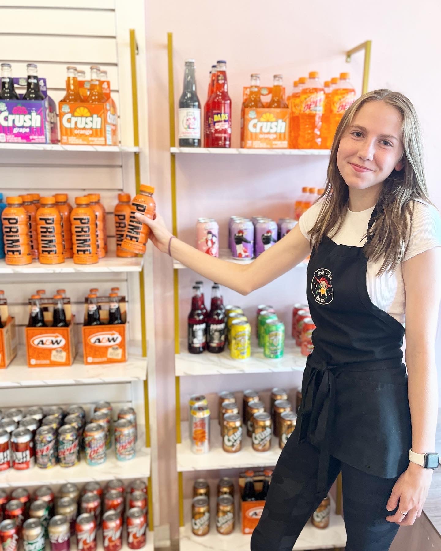 A smiling young woman stocking a shelving unit of beverages with orange prime hydration.