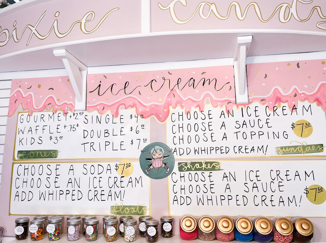 A pink and white ice cream sundae bar menu on the wall of a candy shoppe.