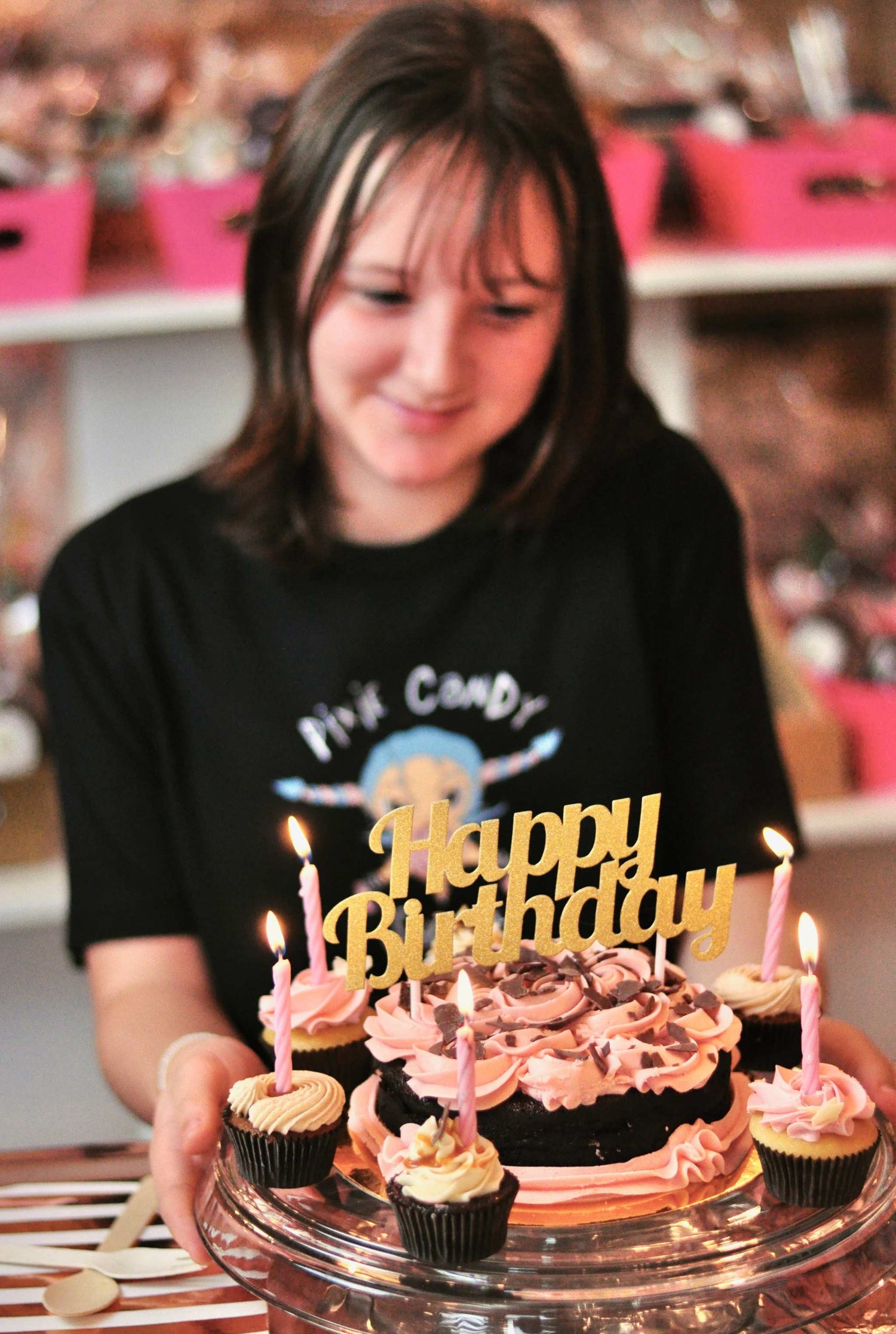 a young caucasian girl with short brown hair looking down at a birthday cake and smiling.