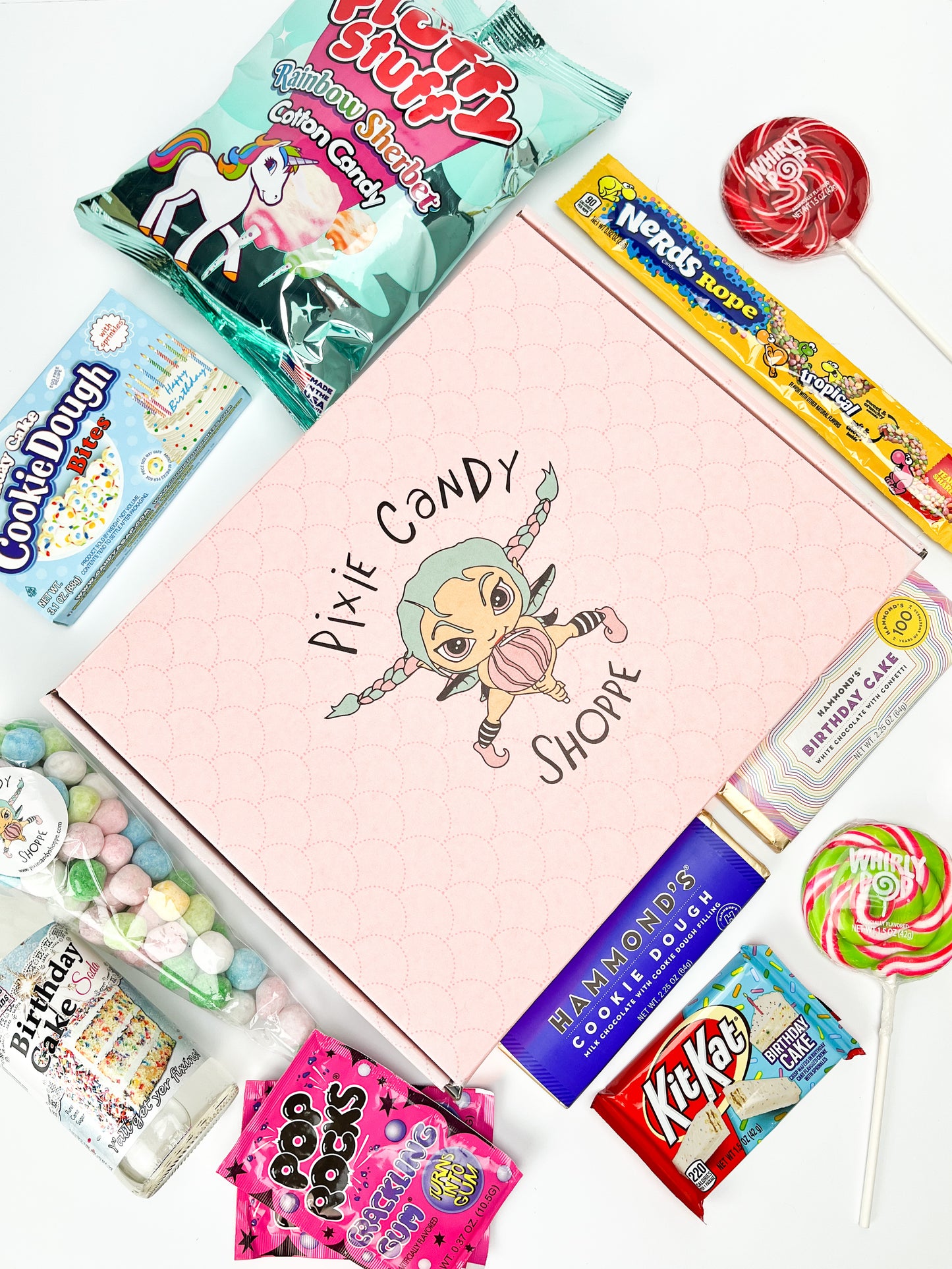 A birds eye view of a pink pixie candy branded box surrounded with birthday themed treats and candy on a white background.