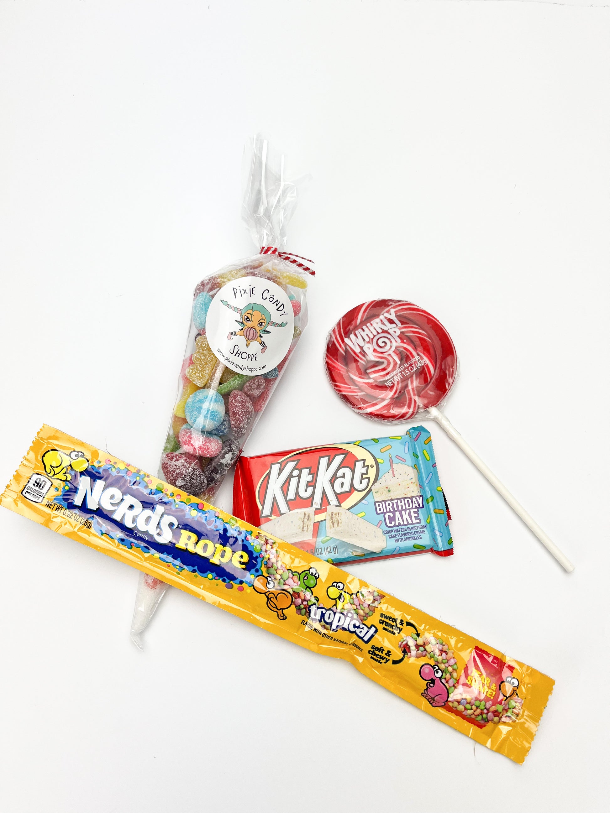 A nerds rope candy, birthday cake kitkat bar, whirly pop, and clear bag of sour candies displayed on a white background.