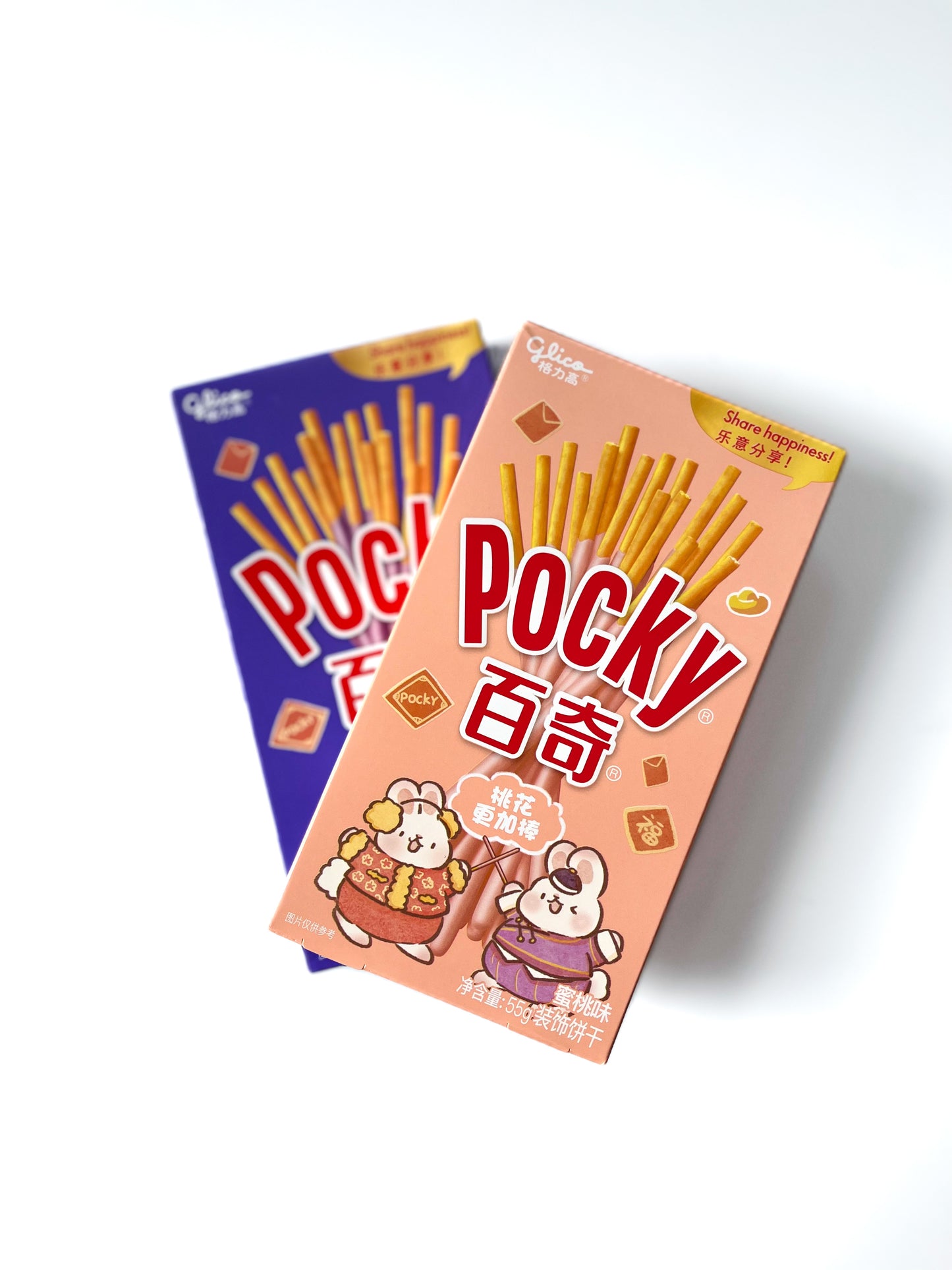A birds eye view of a box of peach pocky biscuits stacked on a box of double berry pocky biscuits on a white background.